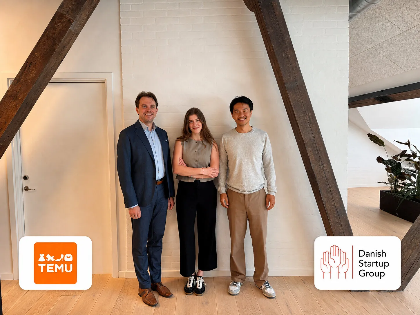 Three people standing indoors between large wooden beams.