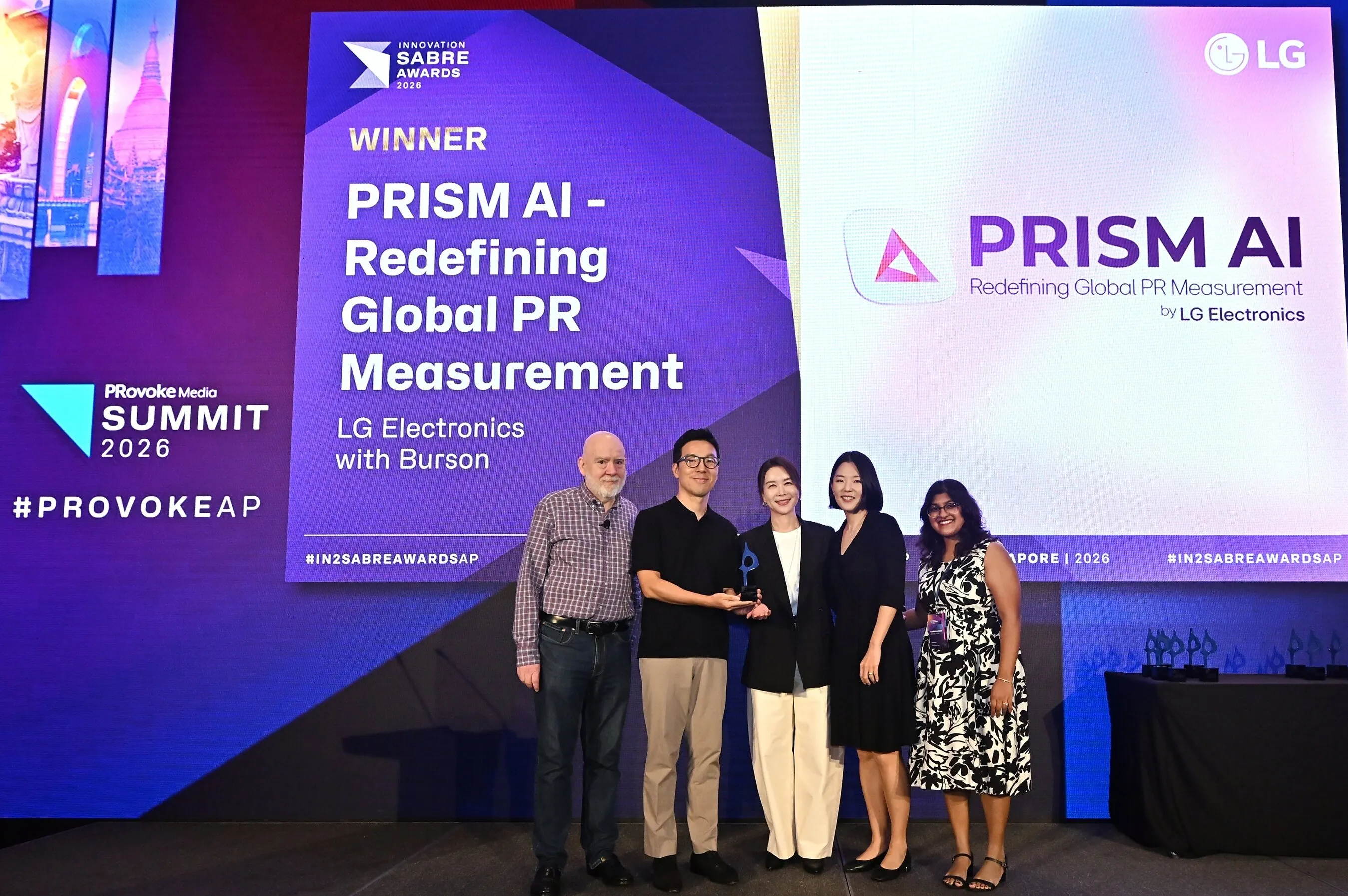 Five people accept an award on stage before screens reading “PRISM AI” and “Winner”.