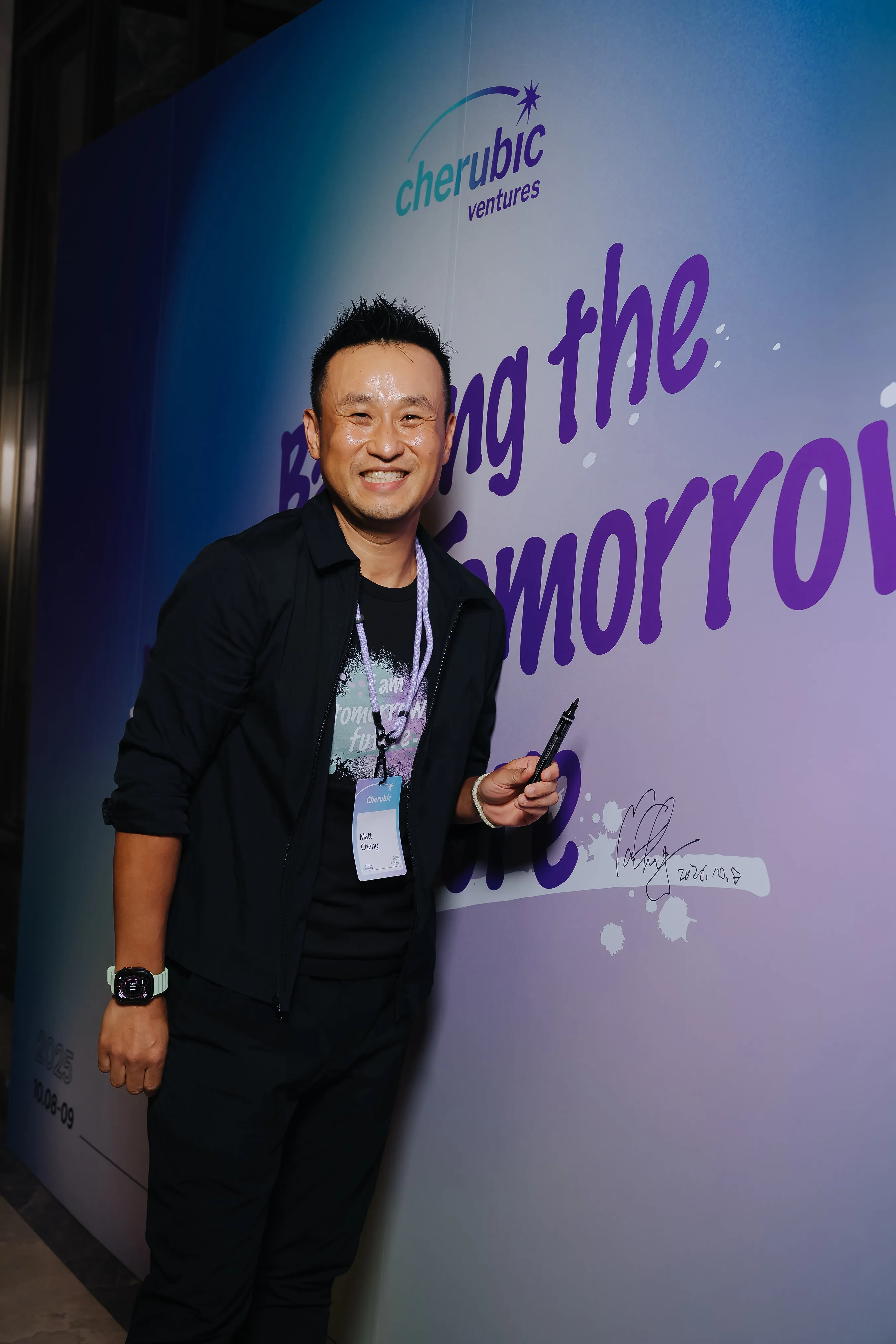 A man holds a marker beside a Cherubic Ventures “Bring the Tomorrow” signing wall.