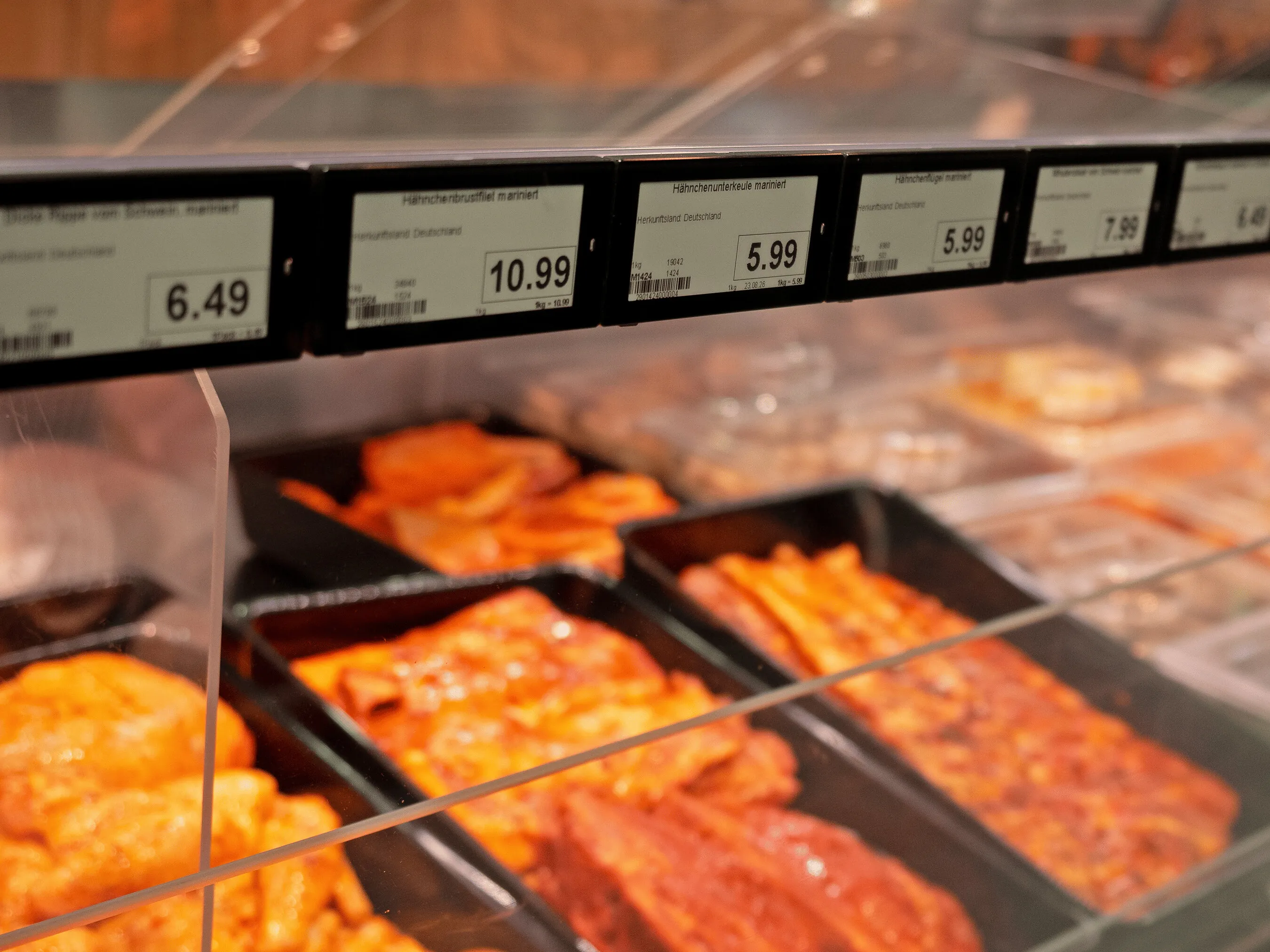 Trays of marinated meat and poultry in a supermarket deli case beneath price labels