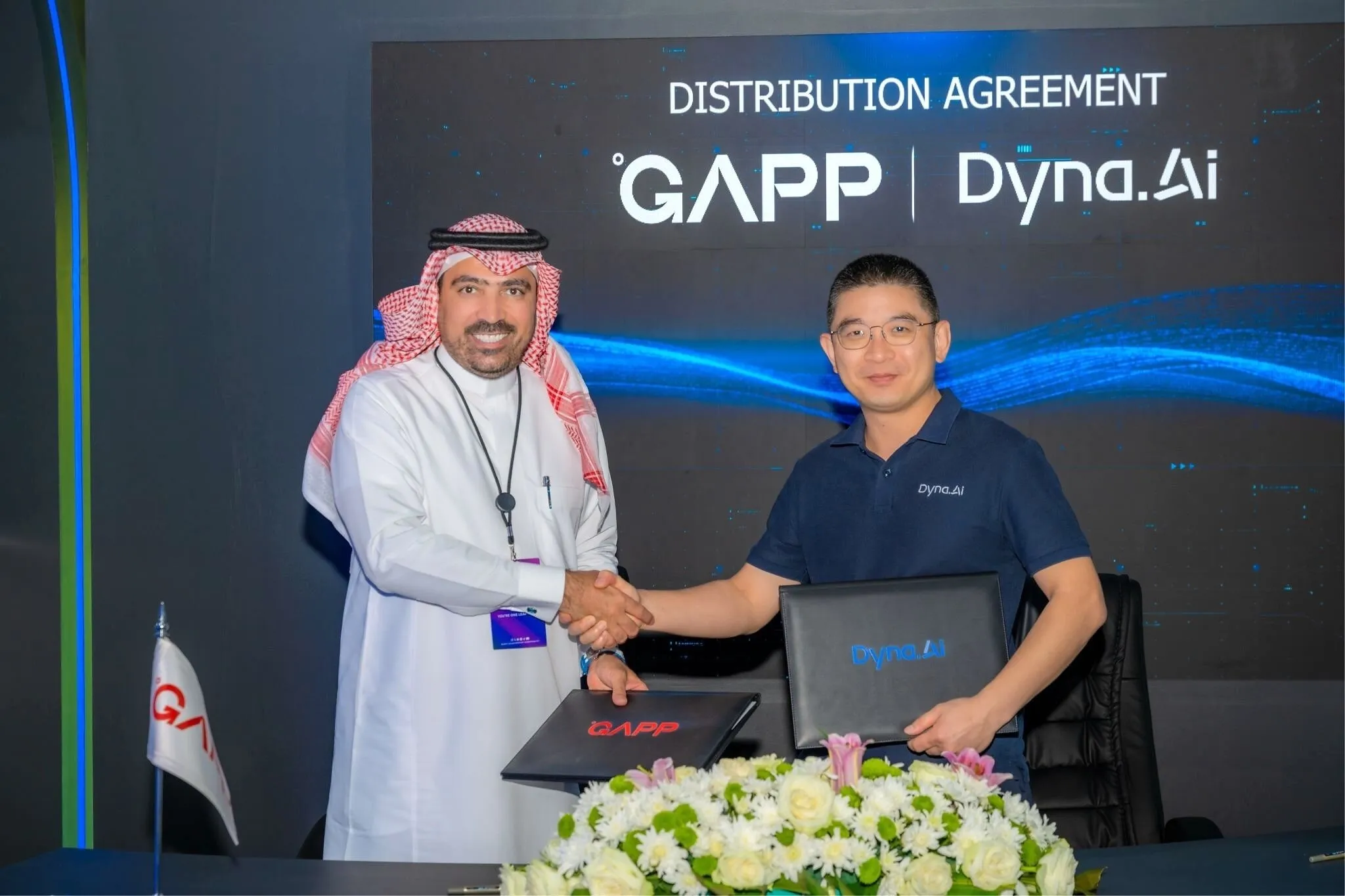 Two men shake hands holding folders before a GAPP and Dyna.AI distribution agreement sign.