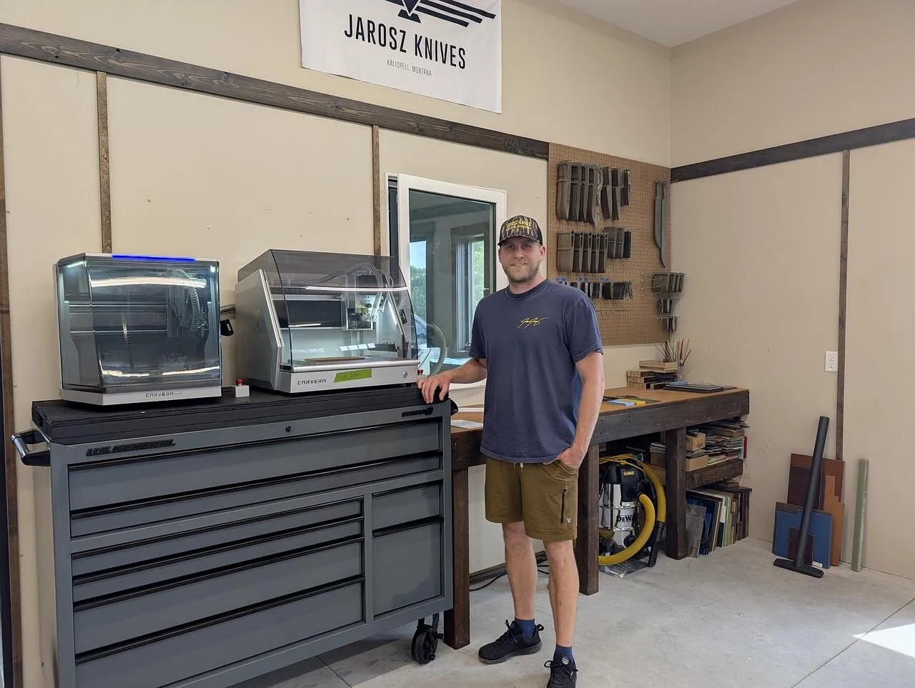 A man stands beside a tool chest topped with two Carvera desktop CNC machines in the Jarosz Knives workshop.