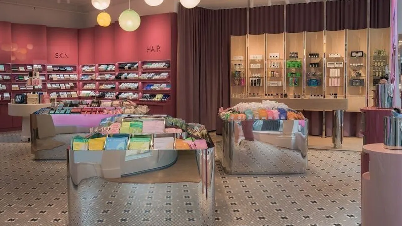 Shelves and mirrored display tables filled with colourful beauty products in a pink shop interior.
