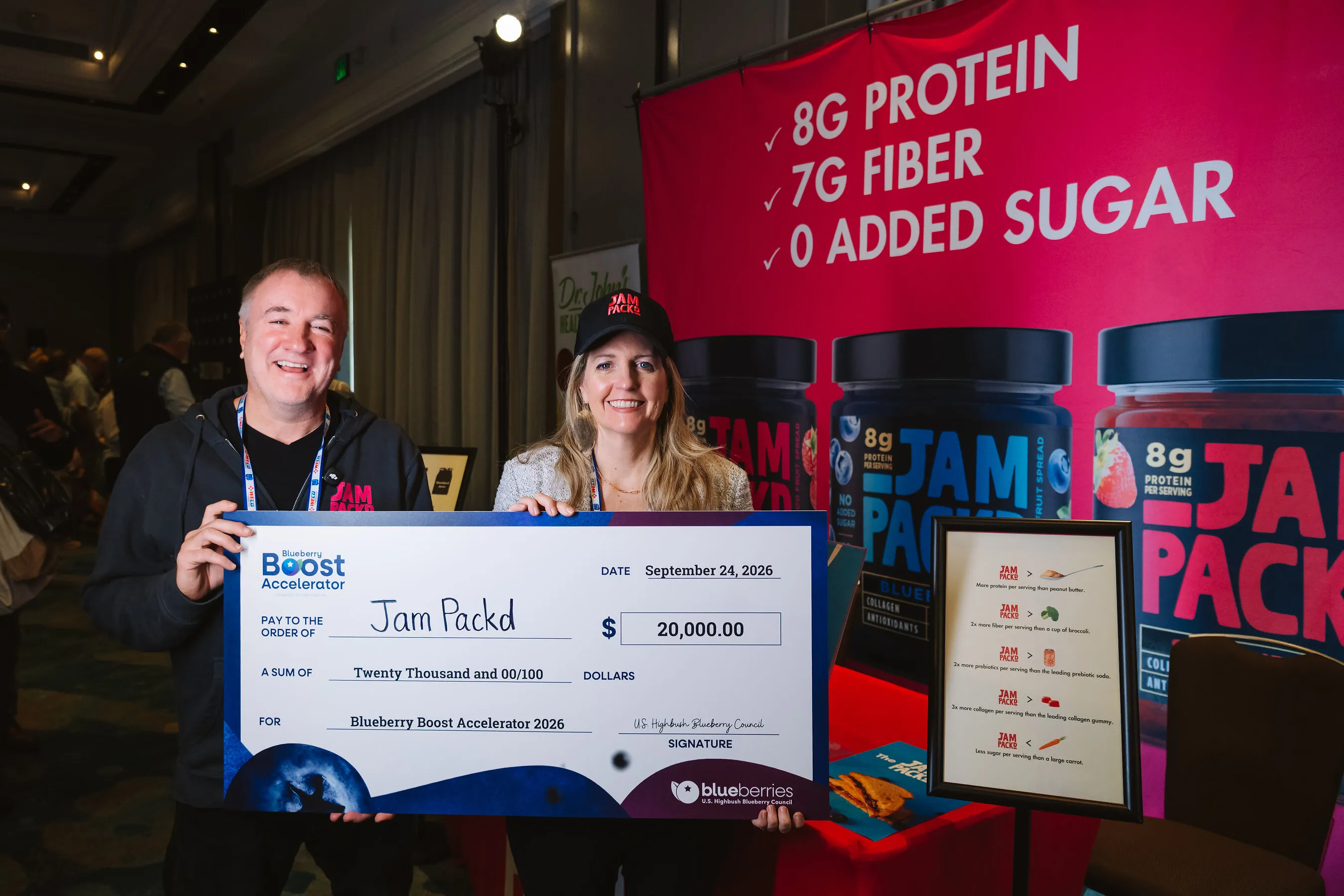 Jam Packd founders Brian and Michelle Platt hold a $20,000 check beside a display of protein jam jars.