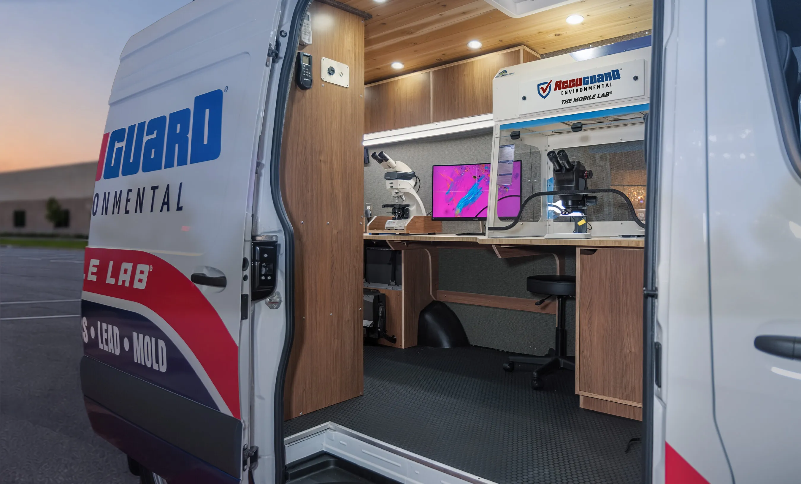 AccuGuard Environmental mobile laboratory van with microscopes and workstations inside at dusk.