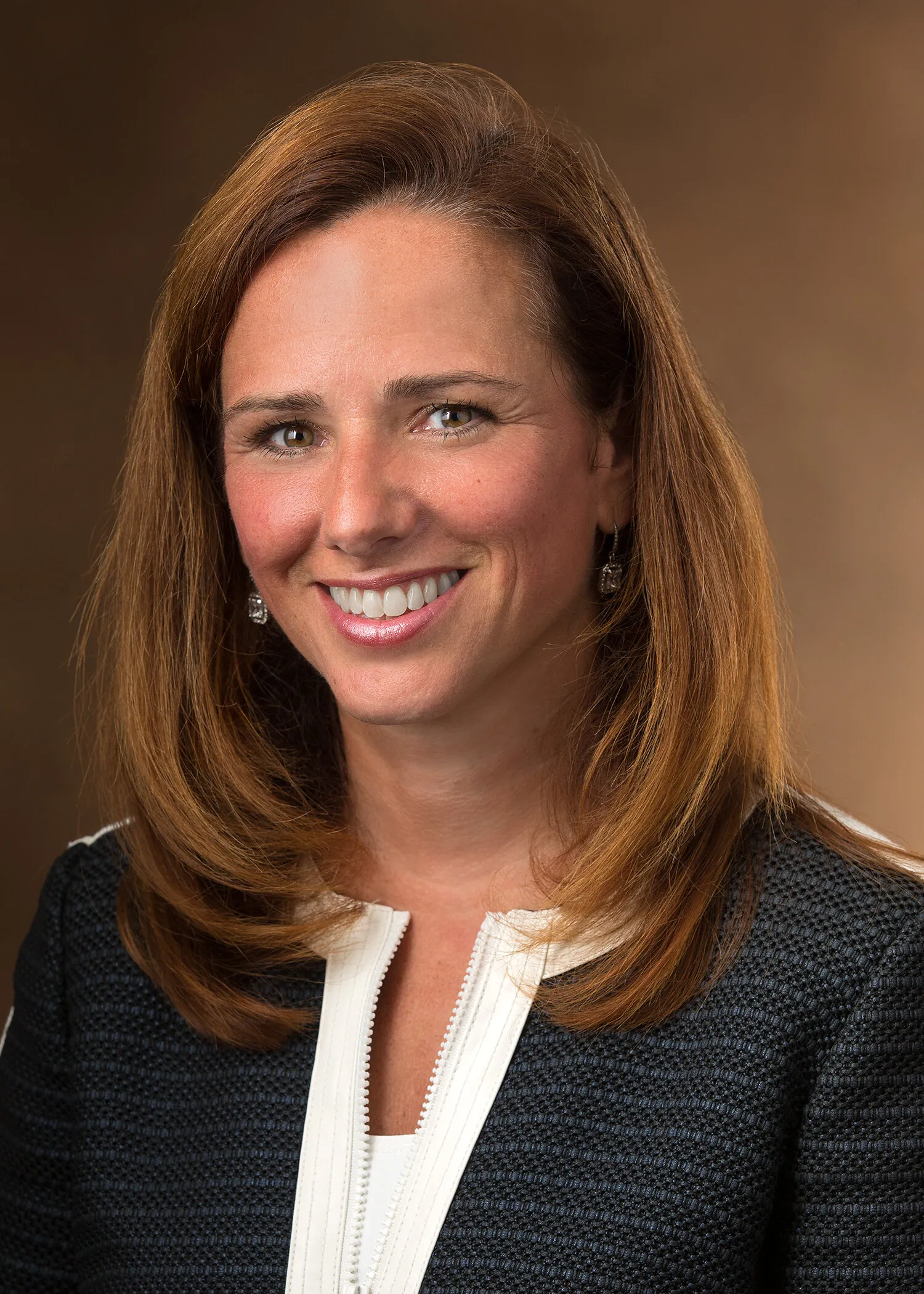 A smiling woman with brown hair wearing a black textured jacket with white trim.