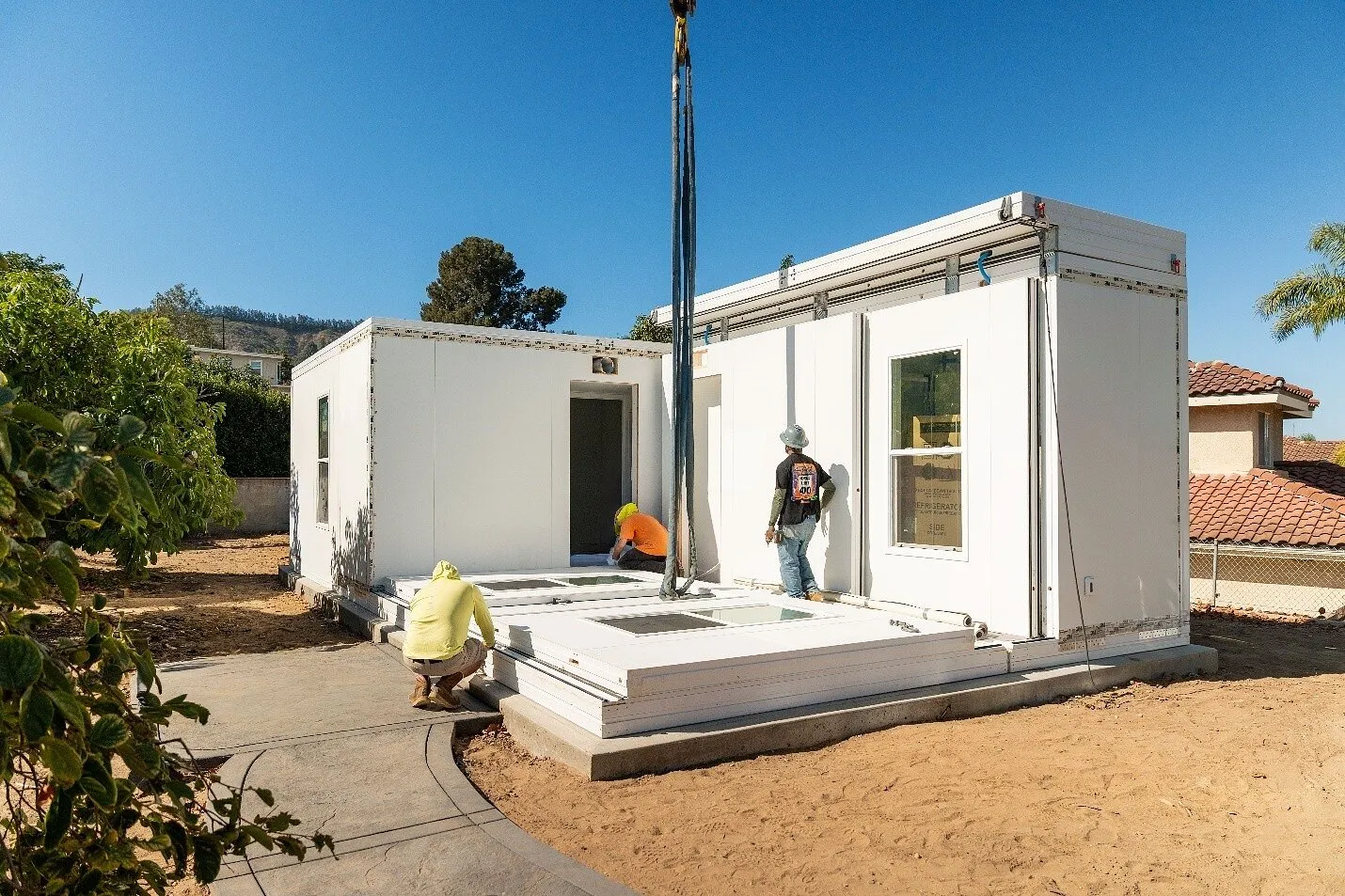 Workers assembling a white prefabricated casita on a concrete foundation.
