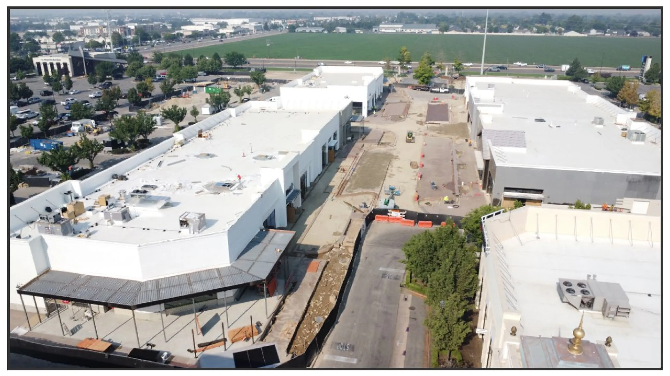Aerial view of white commercial buildings under construction beside a road and green field.
