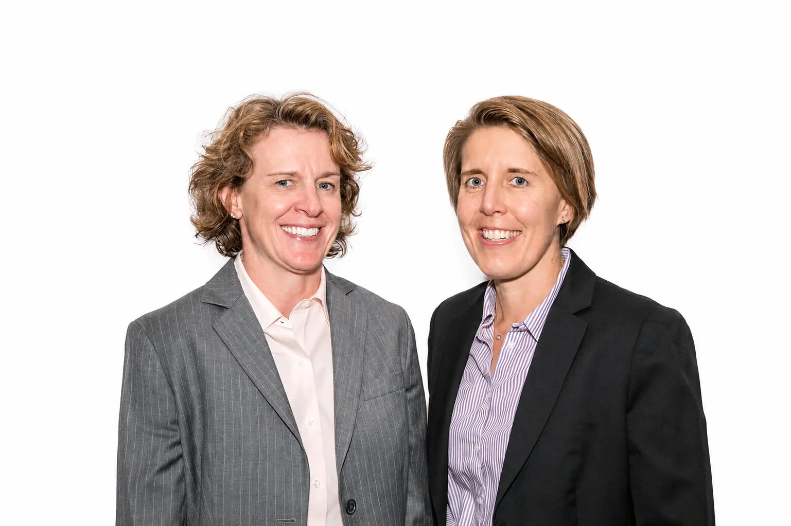 Two women in business suits smiling against a white background.