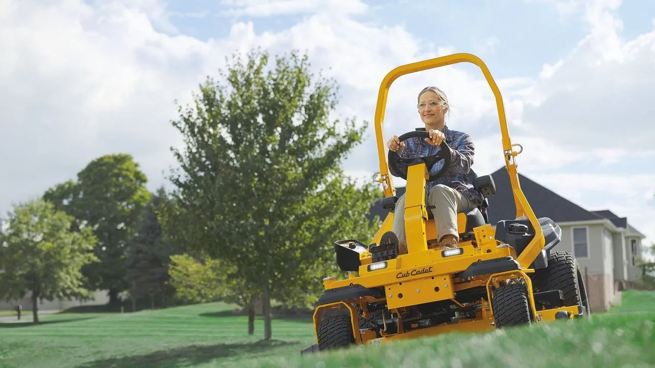 A person rides a yellow Cub Cadet zero-turn lawn mower across a grassy yard.
