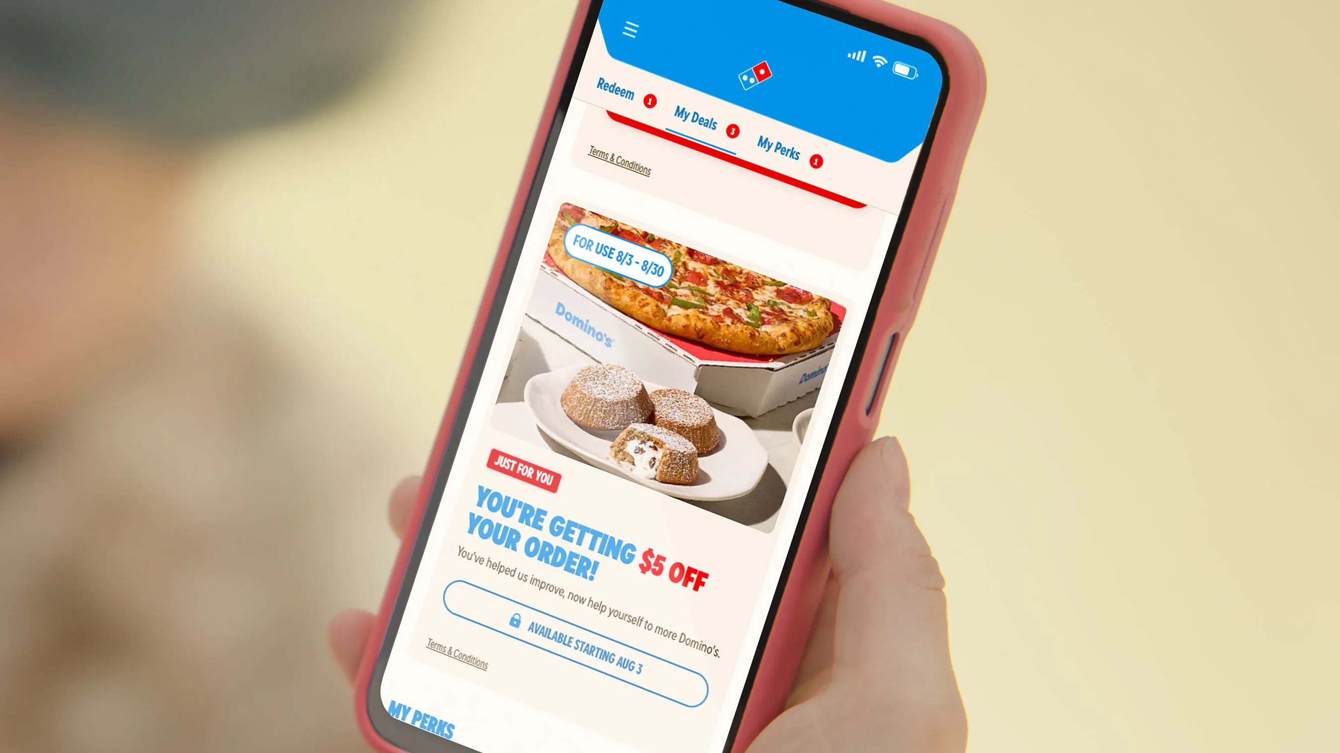 A hand holds a phone displaying Domino’s app offers, including a $5 off reward.