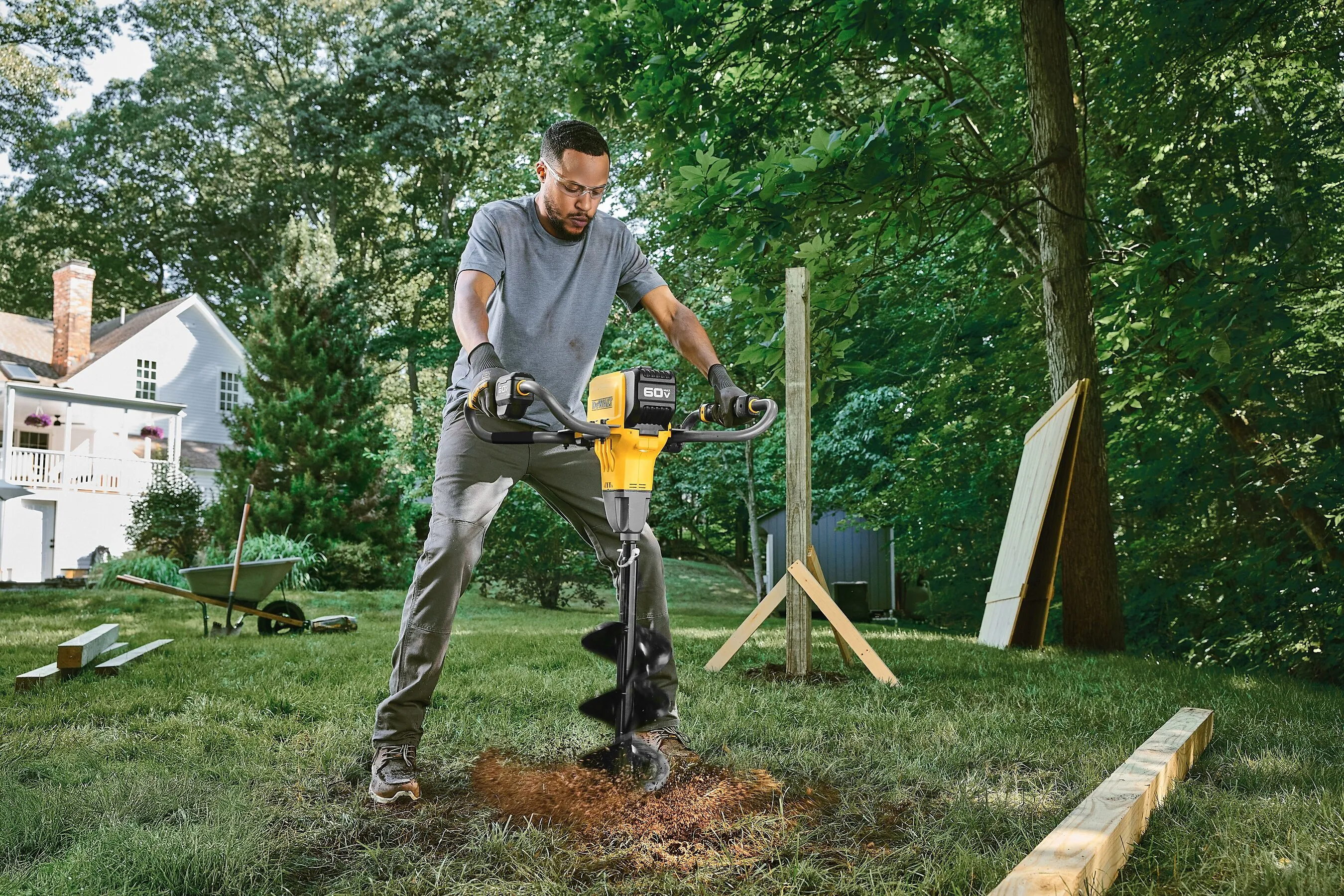 A person uses a cordless auger to dig a hole in a grassy backyard.