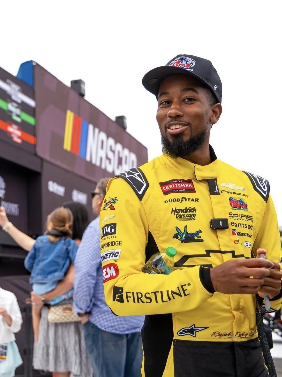 Rajah Caruth in a yellow racing suit and cap at a NASCAR event.