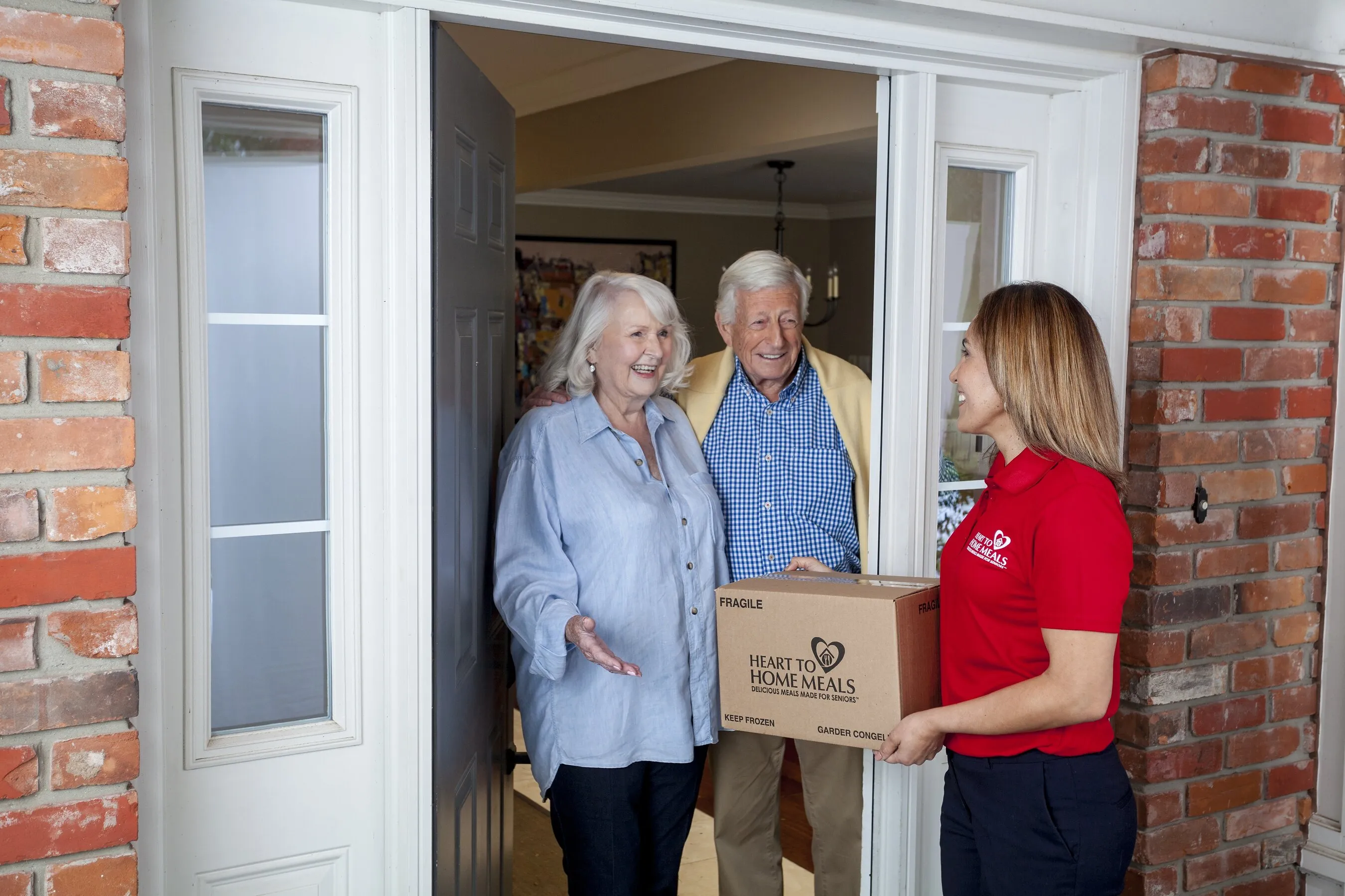 A delivery worker hands a Heart to Home Meals box to an older couple at their front door.