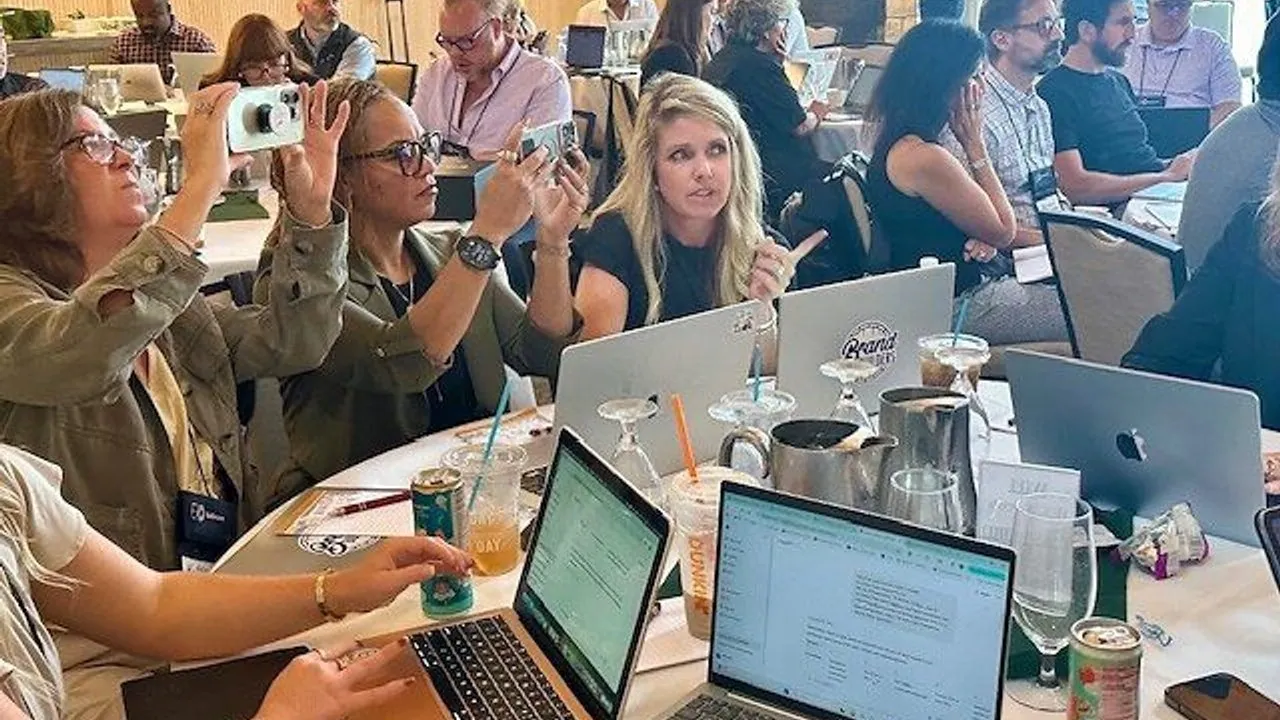 People at a conference table using laptops and phones, with drinks and notebooks.
