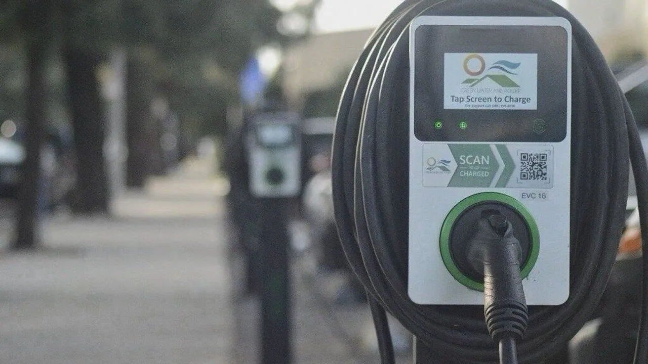 Electric vehicle charging station with a plugged-in cable and QR code label.