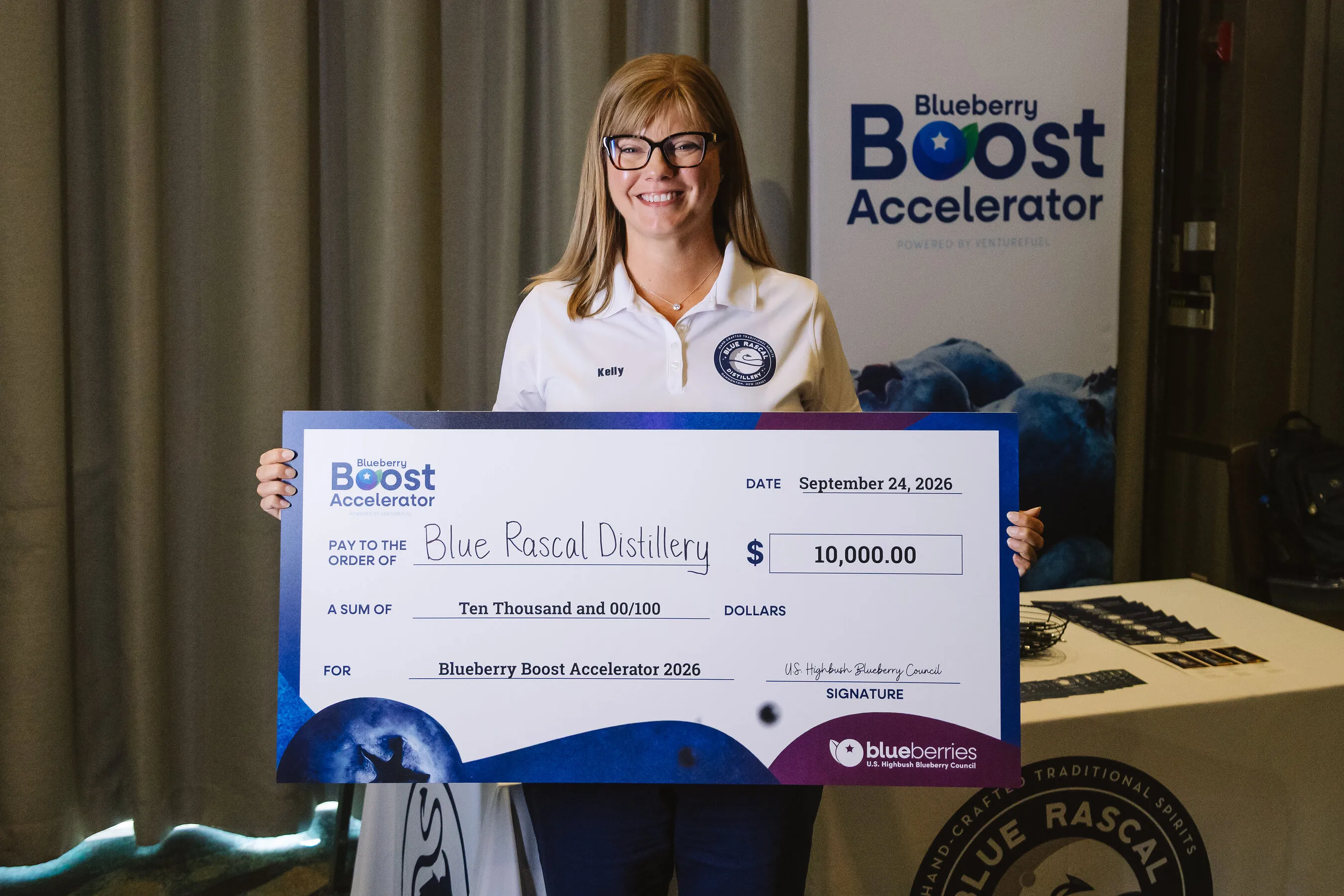 Kelly Perone holds a $10,000 Blueberry Boost Accelerator check for Blue Rascal Distillery.