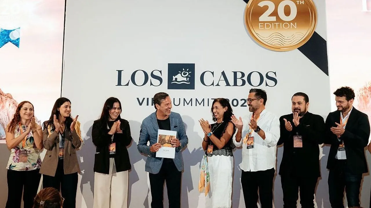 Eight attendees applaud a person holding an award certificate onstage beneath a Los Cabos sign.
