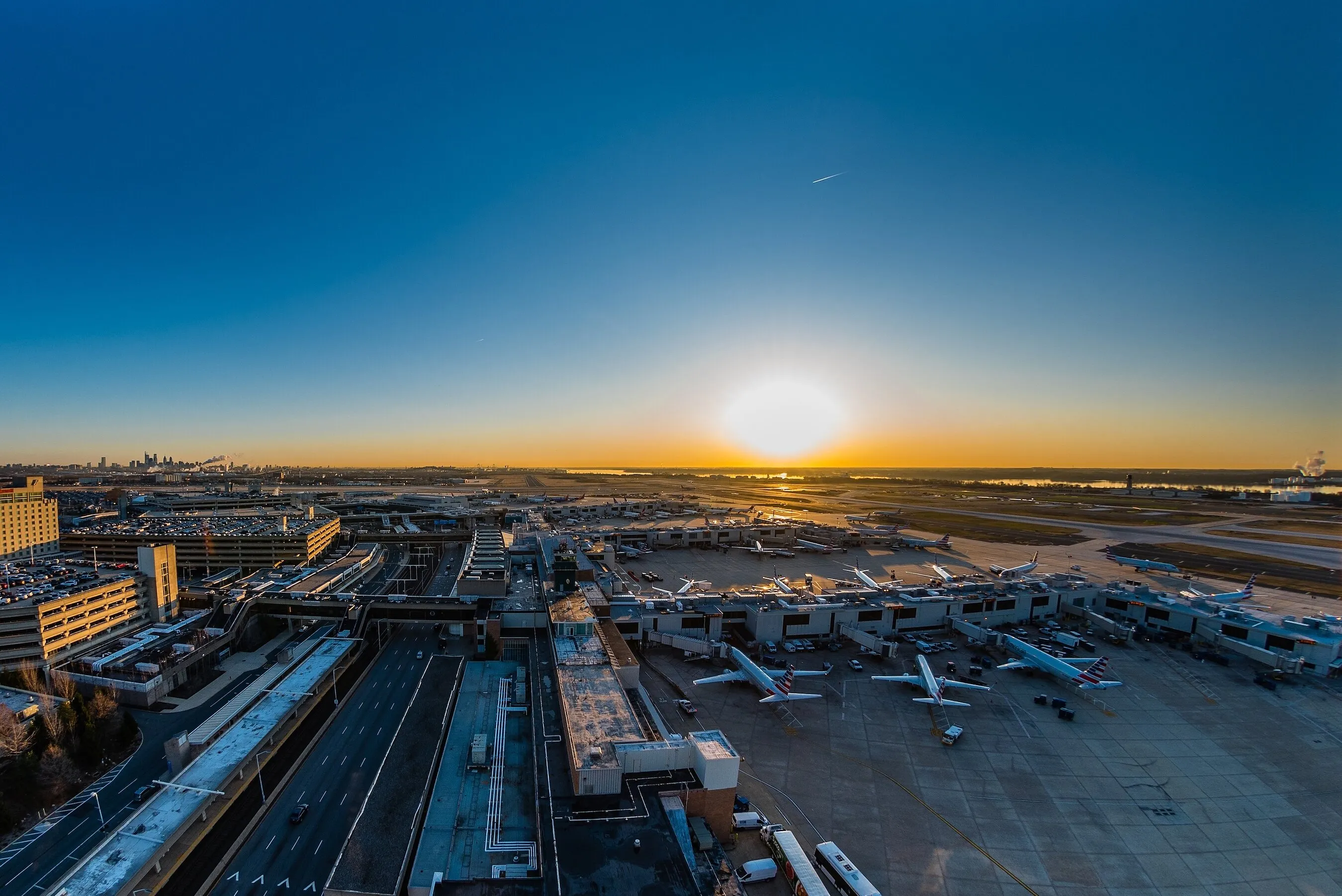 Sunset over an airport terminal with parked planes and runways.