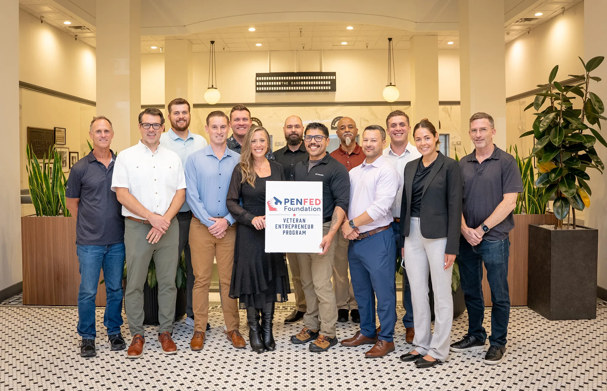 Thirteen people pose with a PenFed Foundation Veteran Entrepreneur Program sign in a lobby.