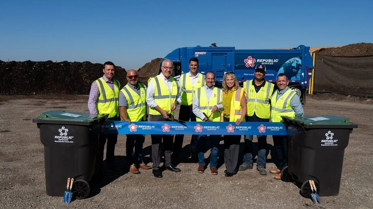 Officials in safety vests cut a ribbon between compost bins at a landfill.