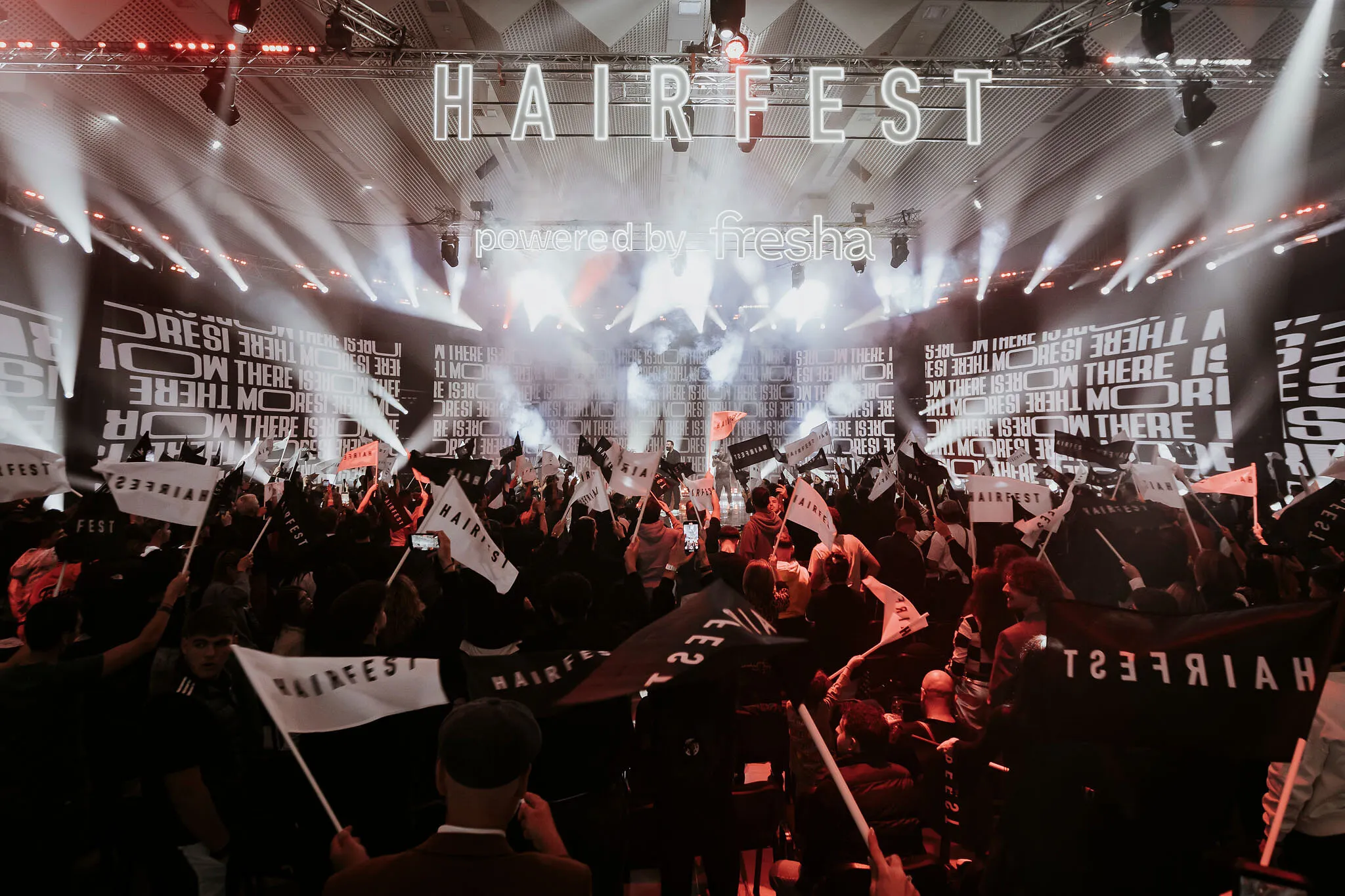 Crowd waving Hairfest flags beneath a brightly lit stage at an indoor event