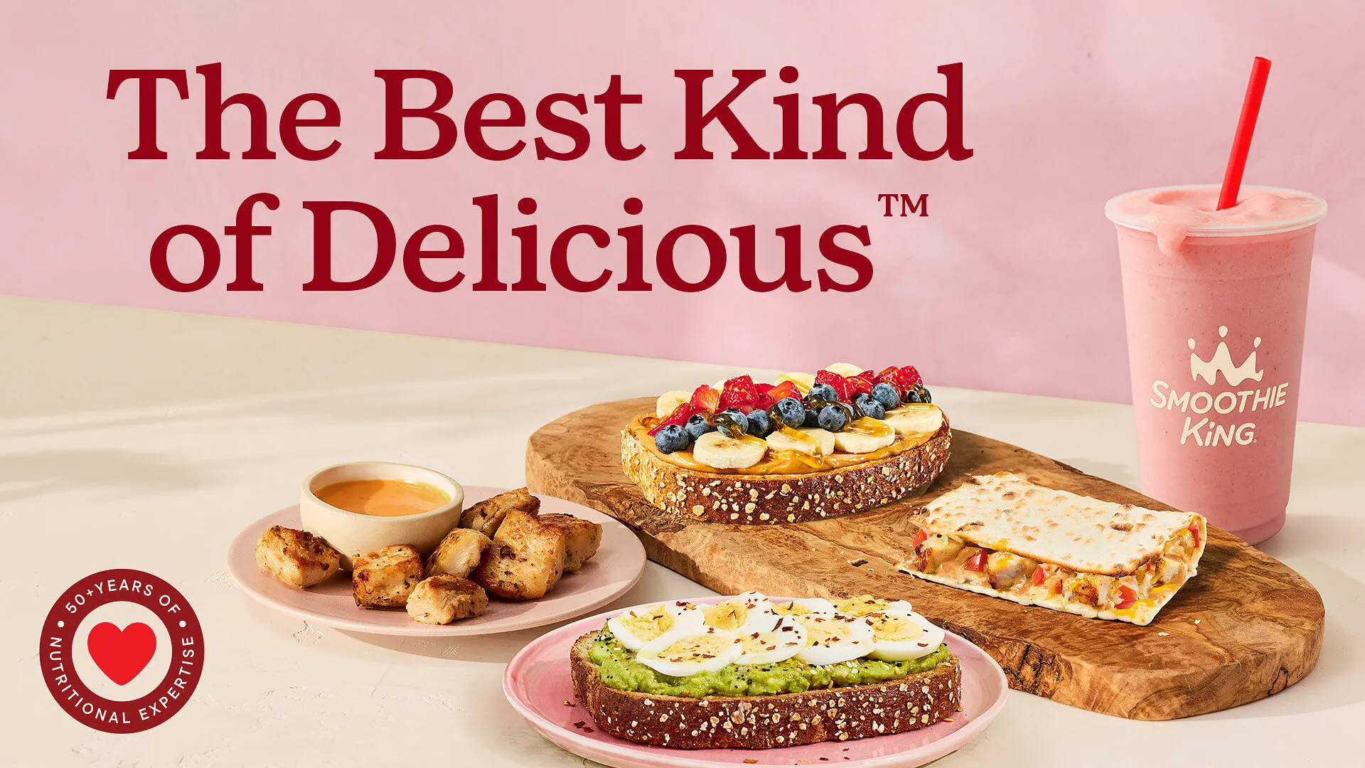 Smoothie King toasts, chicken bites, a flatbread and a pink smoothie beneath “The Best Kind of Delicious” text.