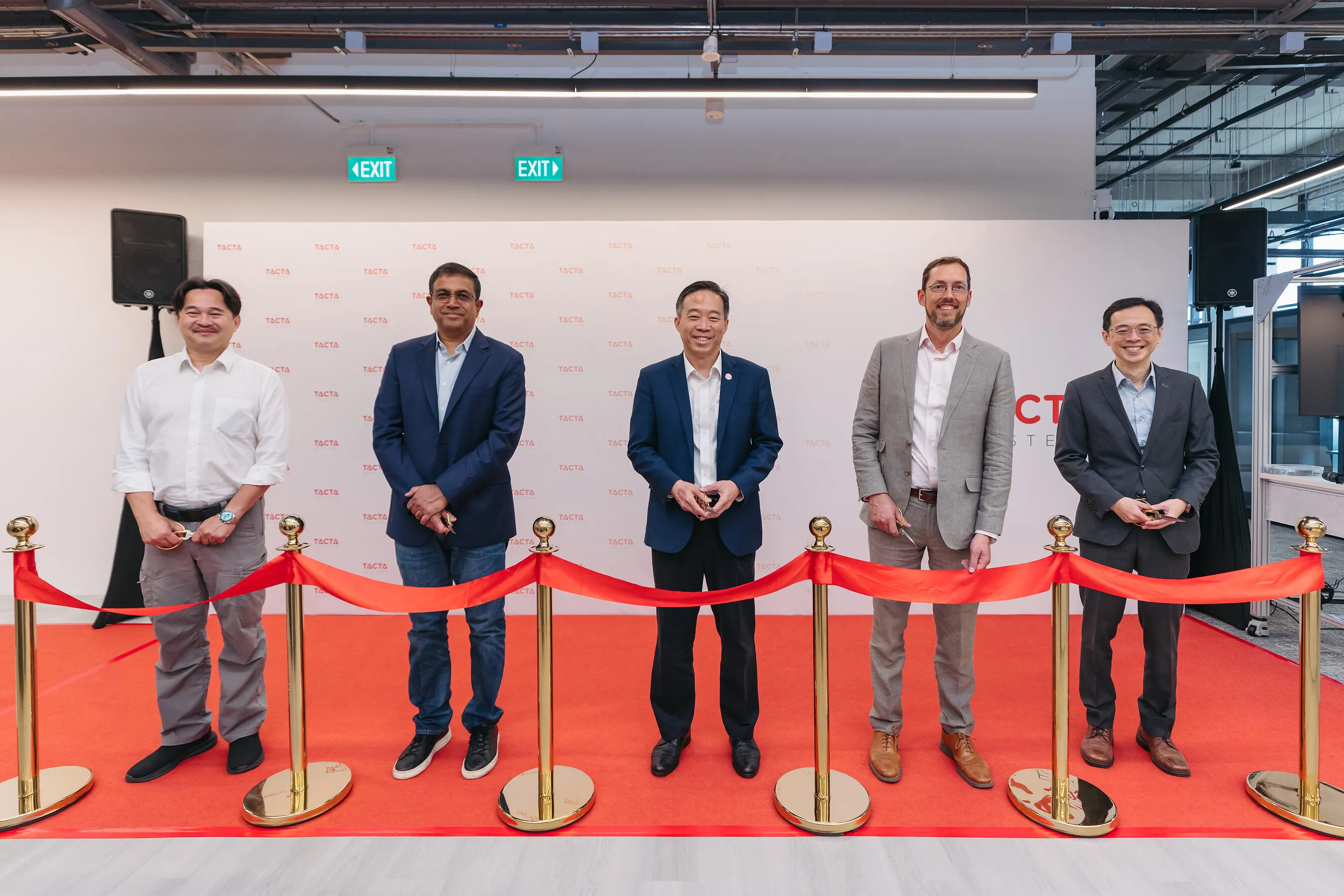 Five men stand behind a red ribbon with scissors at a Tacta Systems event.