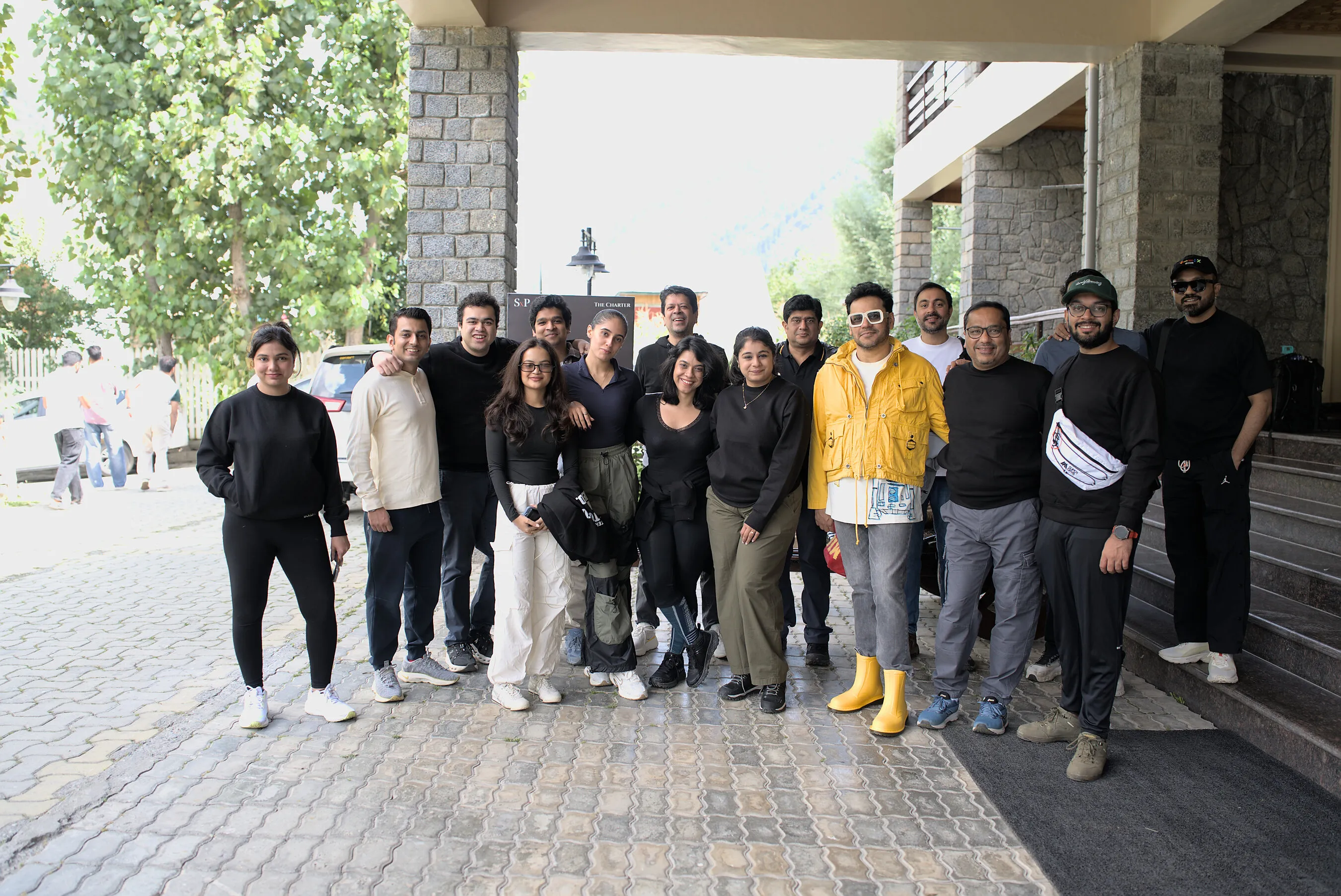 A group of people posing outside a stone building, with one man wearing a yellow jacket and rain boots.