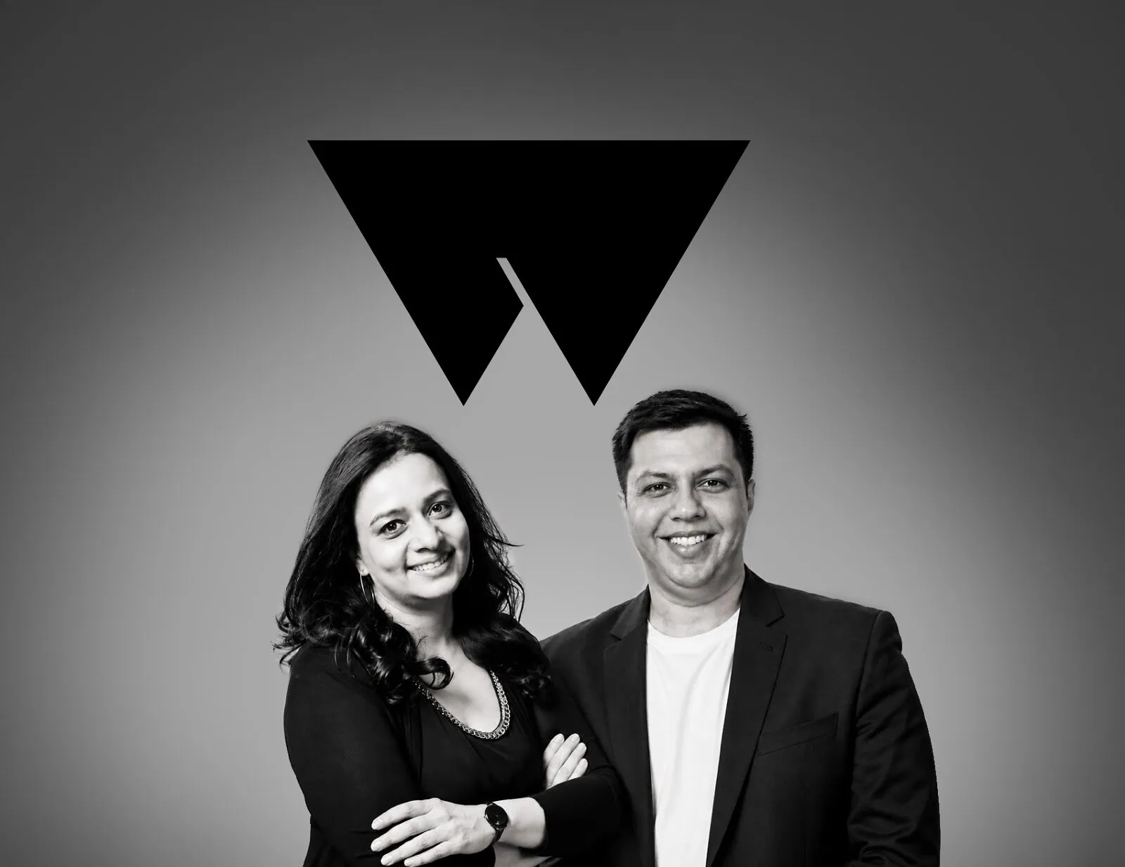 Vandana and Shidush standing beneath a black geometric logo.