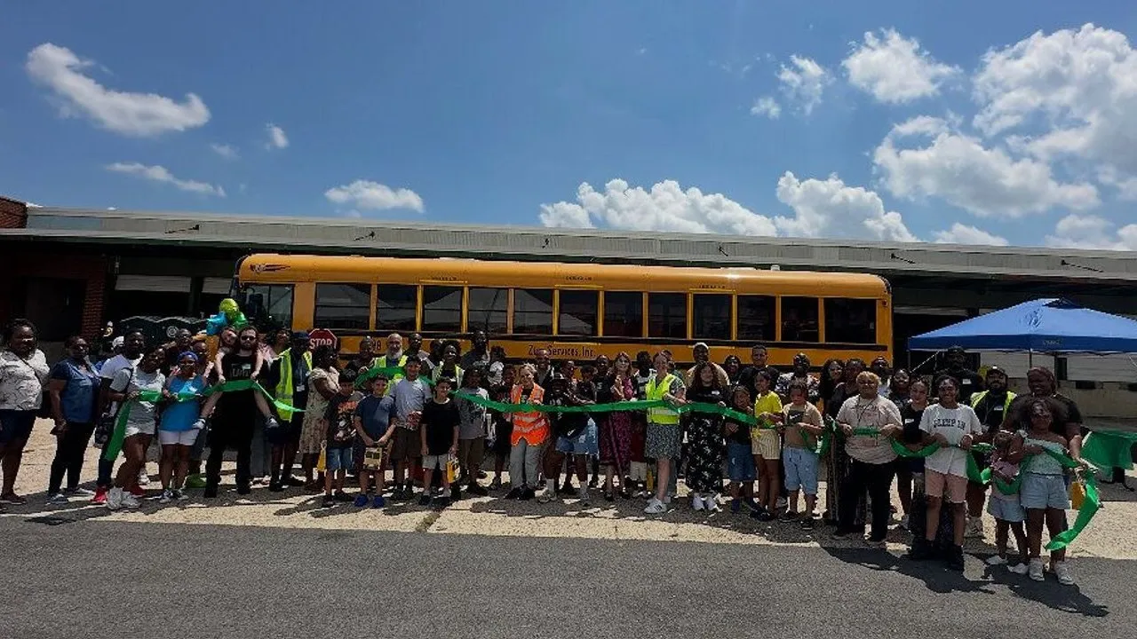 A group stands with a green ribbon in front of a yellow school bus.