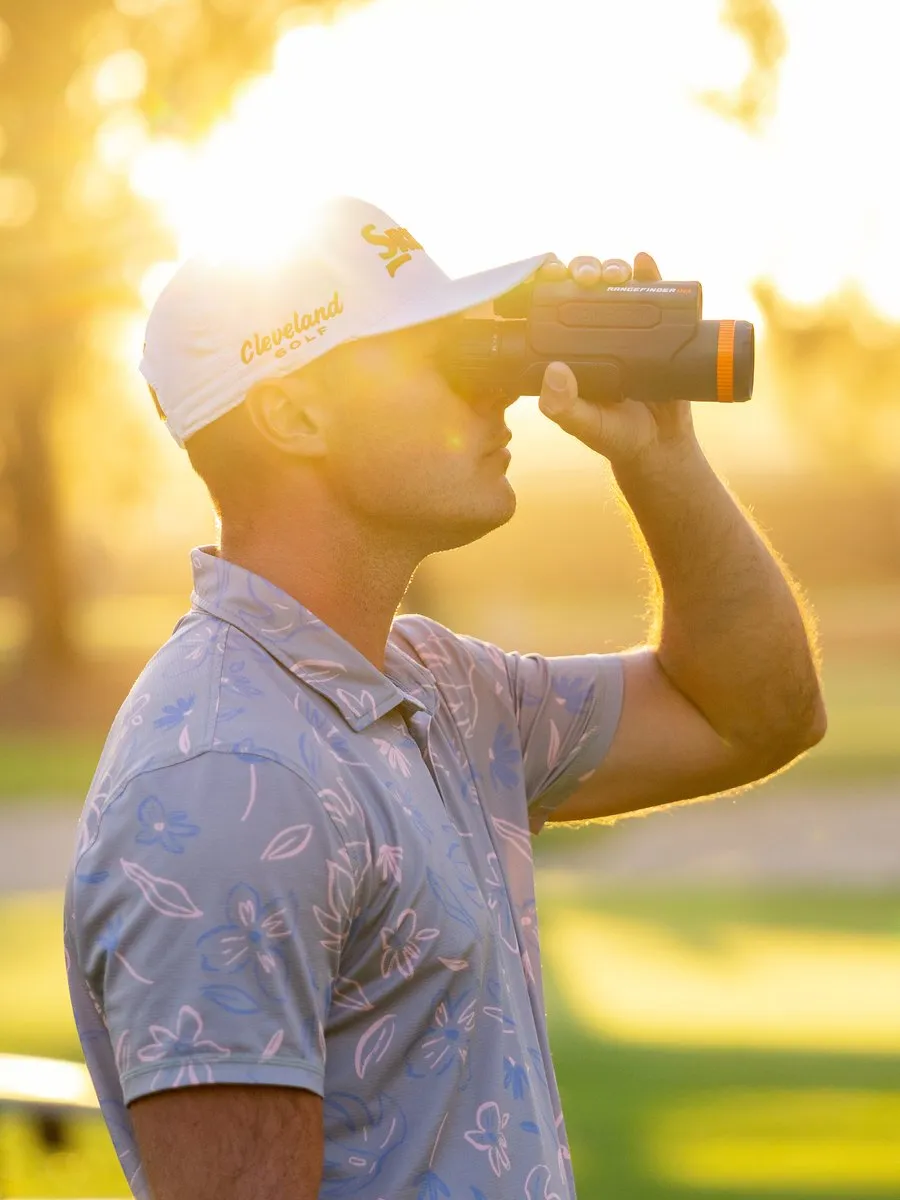 A golfer uses a rangefinder while standing on a sunlit course.